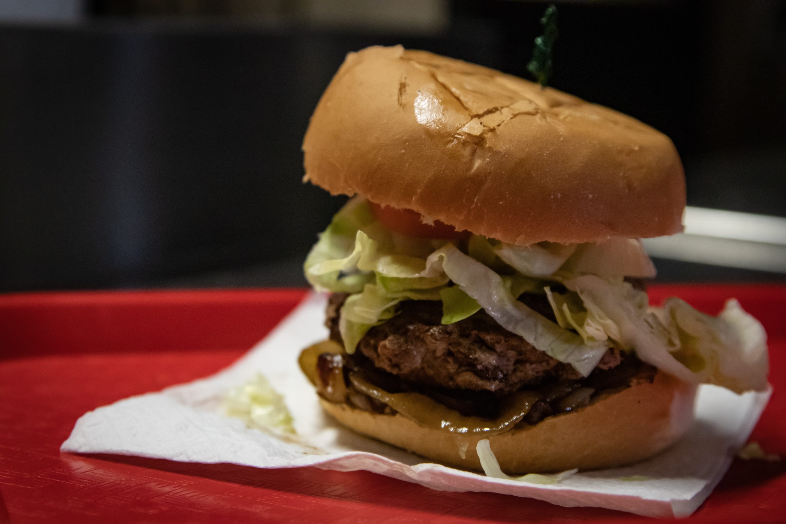 A homemade burger with lettuce and fried onions on a red tray at MJ's Own Munchies