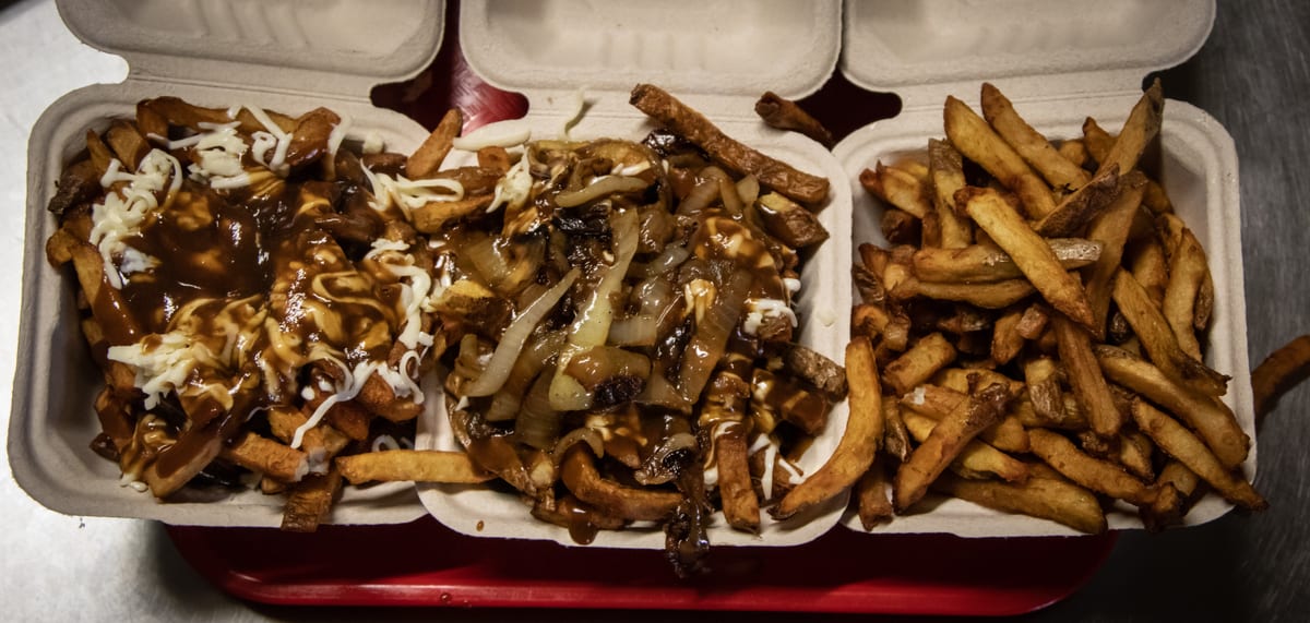 Poutine with fried onions beside a box of fresh cut fries